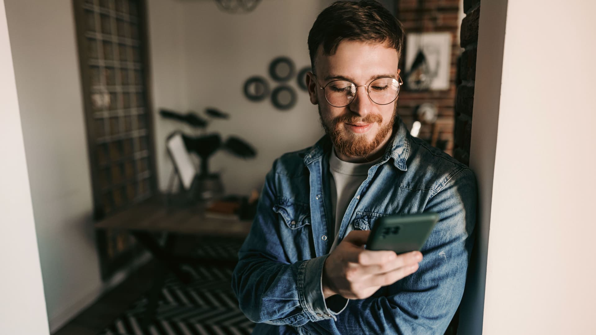Junger Mann lehnt in einem Türrahmen und blickt in sein Smartphone