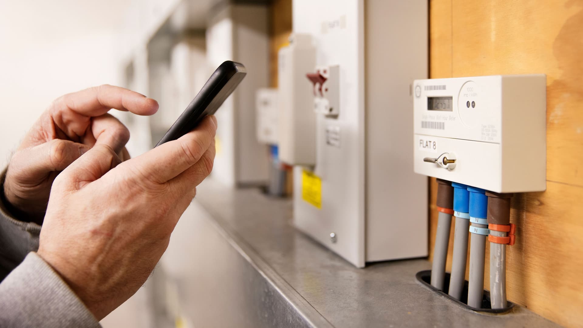 Mann liest digitalen Stromzähler per Smartphone ab – Beispiel für smarte Haustechnik im Eigenheim