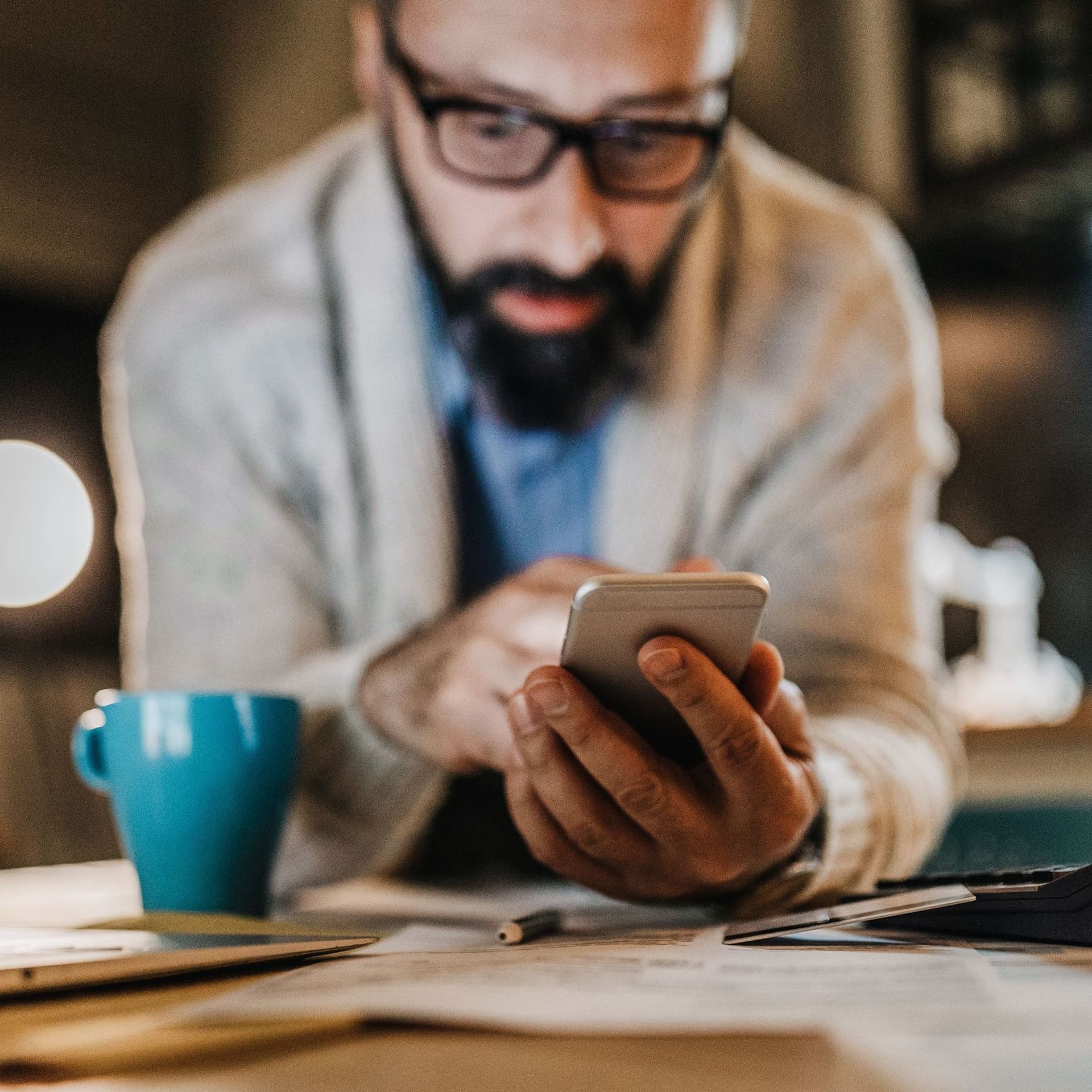 Mann mit Brille und Bart ist unschaft im Hintergrund. Im Fokus ist das Smartphone, das er hält und auf das er schaut.