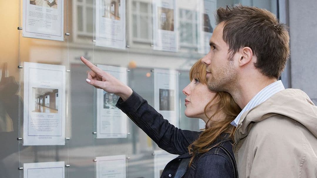 Paar schaut ins Fenster eines Immobilienmaklers