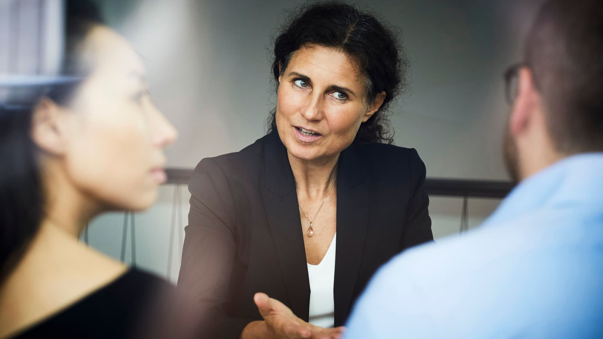 Confident mature female financial advisor discussing with businessman and businesswoman during meeting at office