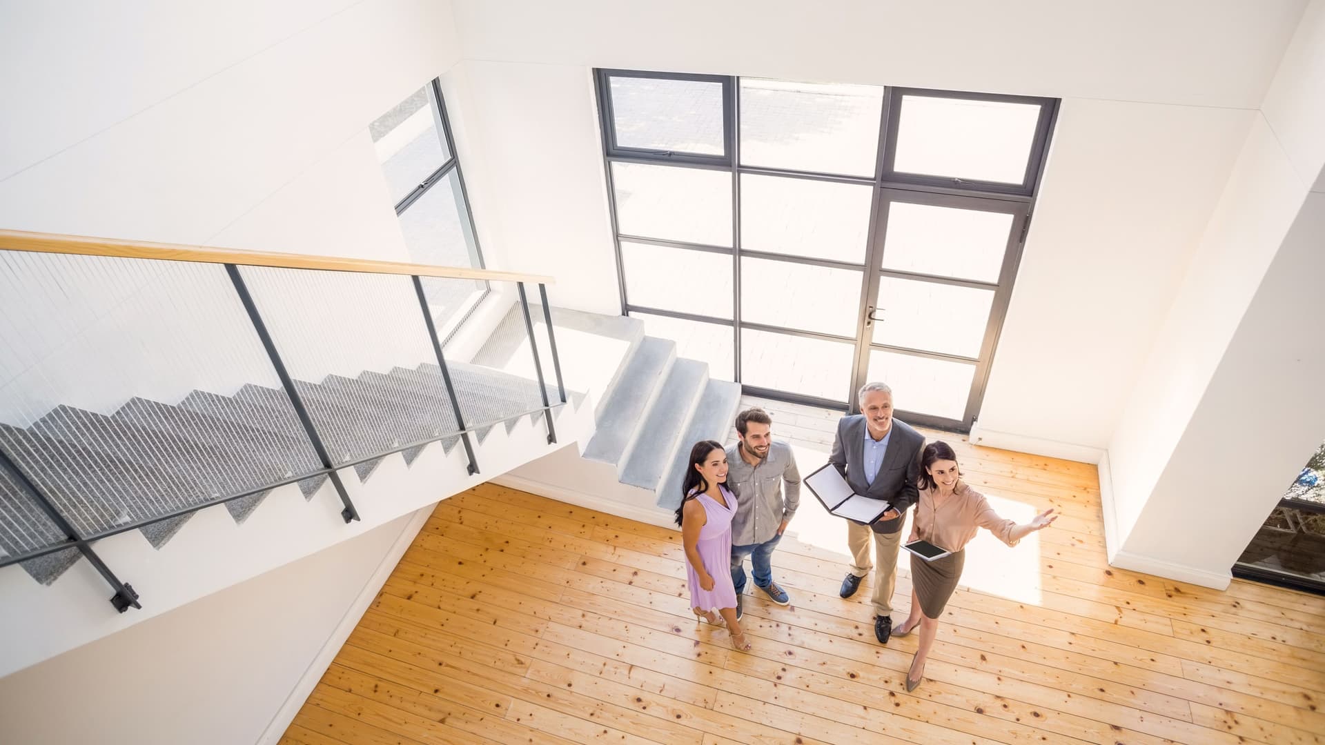 Vogelperspektive einer Maklerin mit drei Immobilienintressenten. Sie steht in offener und moderner Wohnung und gestikuliert.