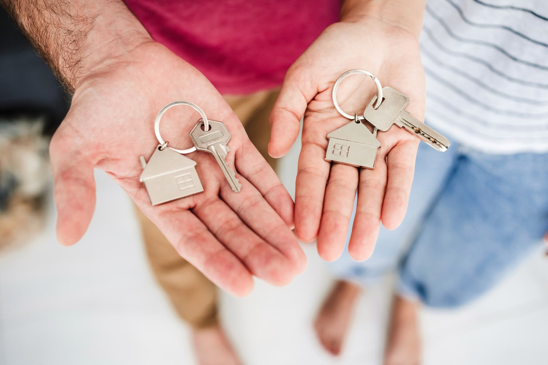 Zwei Personen halten jeweils eine Hand geöffnet, in denen Hausschlüssel mit kleinen Haus-Anhängern liegen.